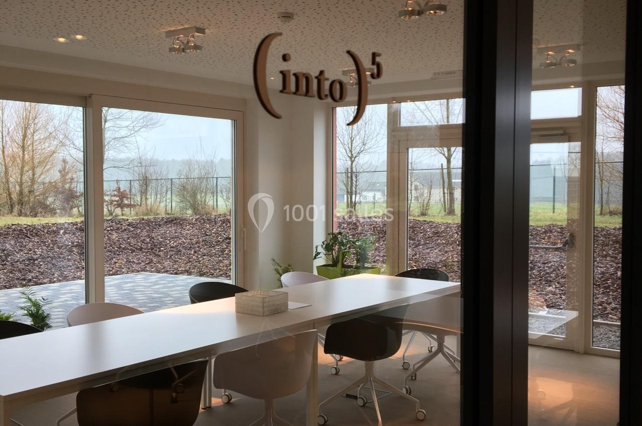 Salle de réunion lumineuse avec une grande table blanche, des chaises à roulettes et des baies vitrées donnant sur un…