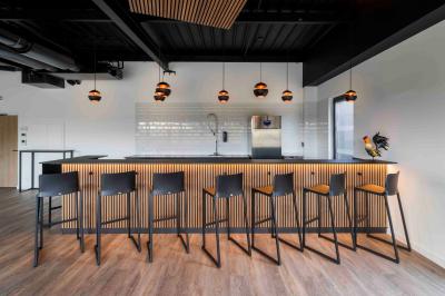 Cuisine moderne avec plancher en bois, tables hautes, chaises noires, réfrigérateur, micro-ondes et cafetière.