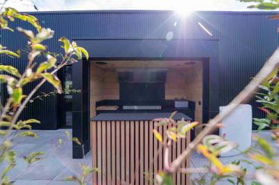 Cuisine moderne avec plancher en bois, tables hautes, chaises noires, réfrigérateur, micro-ondes et cafetière.