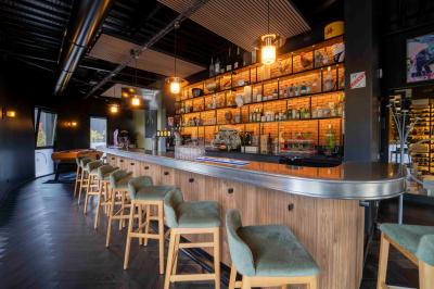 Cuisine moderne avec plancher en bois, tables hautes, chaises noires, réfrigérateur, micro-ondes et cafetière.