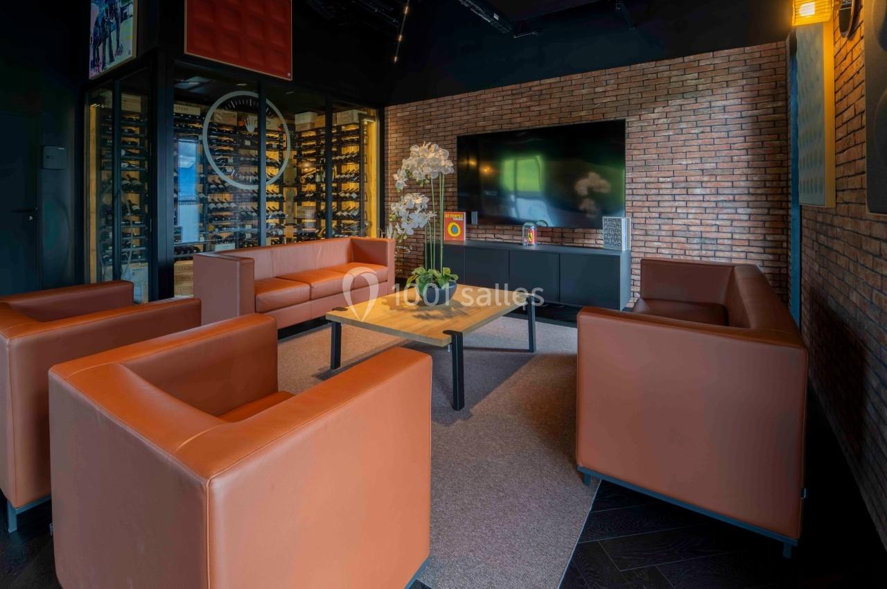 Salle de séjour moderne avec canapés en cuir orange, table basse en bois, écran mural et mur en briques apparentes.
