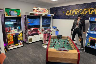 Cuisine moderne avec plancher en bois, tables hautes, chaises noires, réfrigérateur, micro-ondes et cafetière.