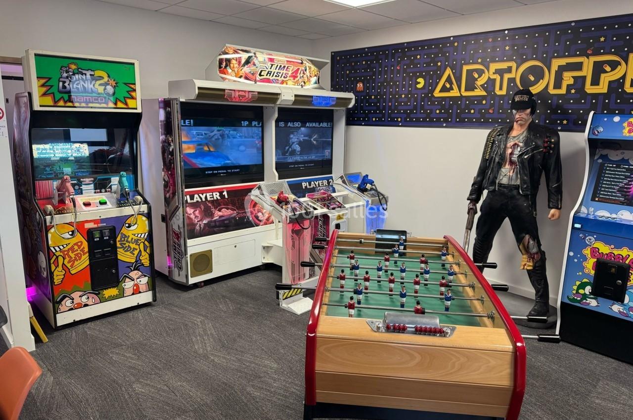 Salle de jeux rétro avec bornes d'arcade, baby-foot, statue décorative et décor mural inspiré de Pac-Man.
