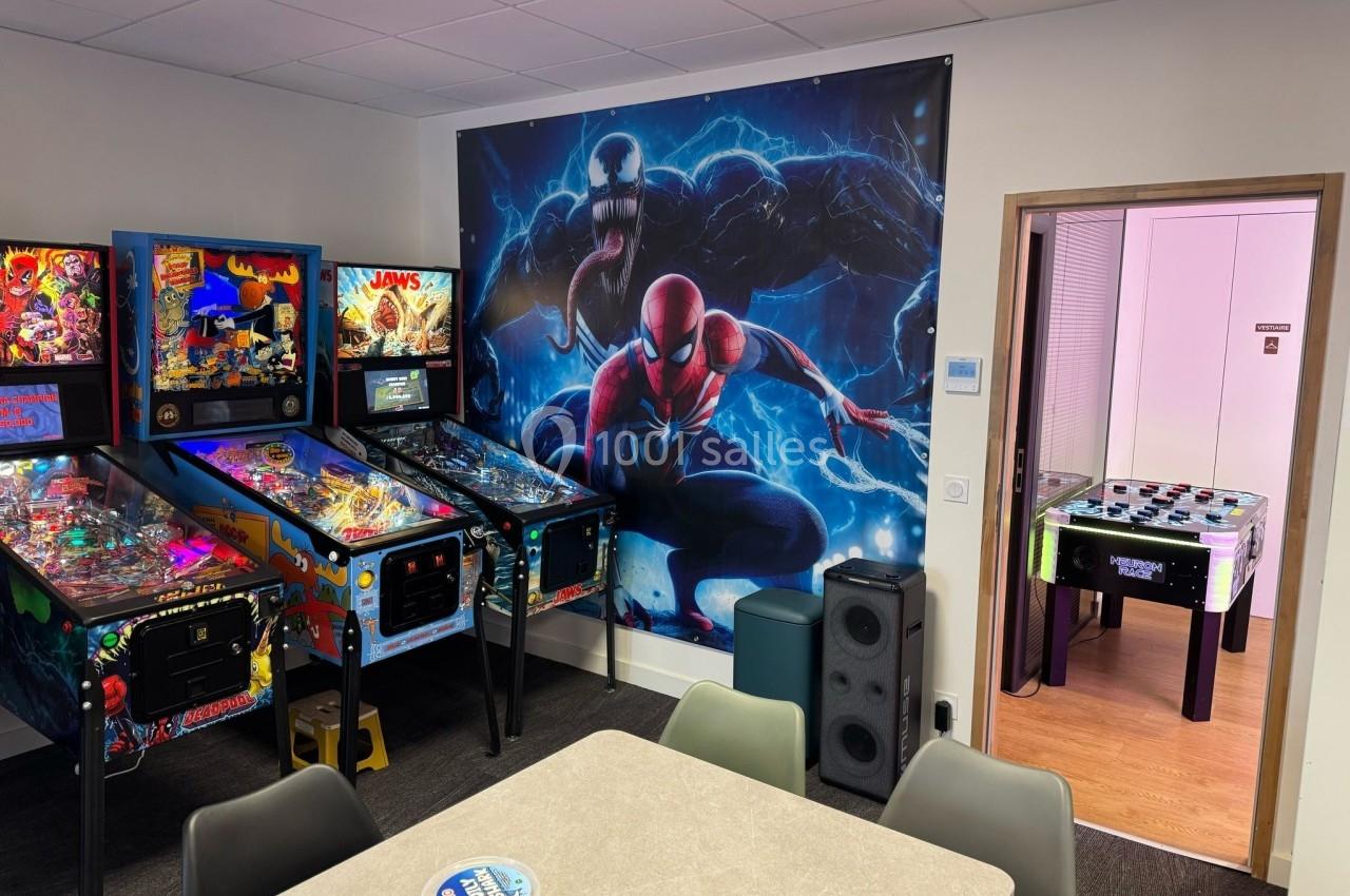 Salle de détente avec flippers, baby-foot et décoration murale représentant Spider-Man et Venom.