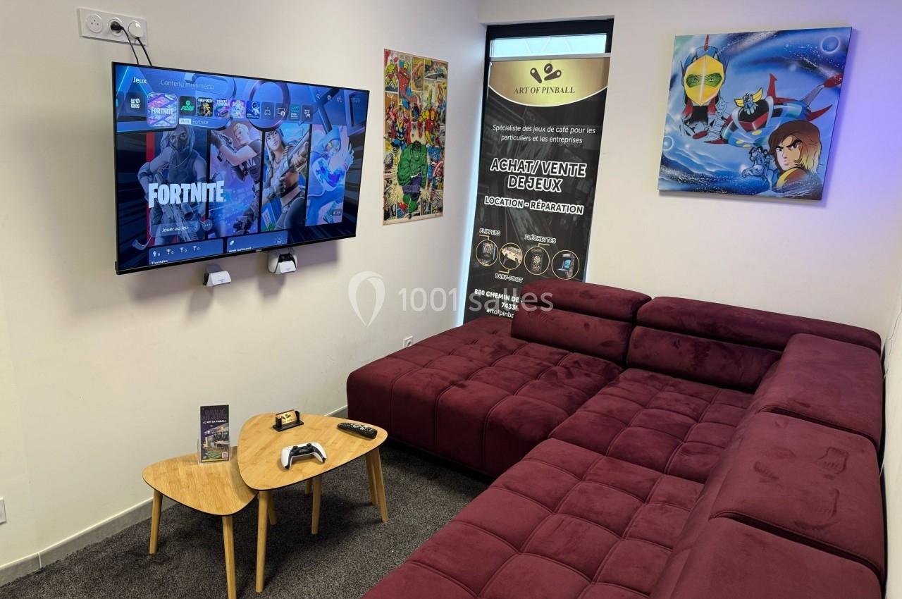 Salle avec canapé d'angle, table basse, écran affichant un jeu vidéo, posters et bannière promotionnelle au mur.