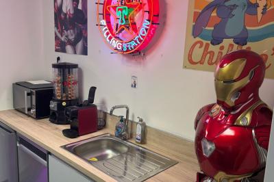 Cuisine moderne avec plancher en bois, tables hautes, chaises noires, réfrigérateur, micro-ondes et cafetière.