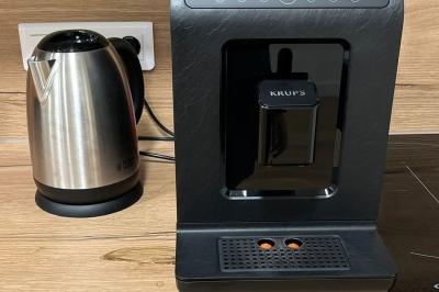 Cuisine moderne avec plancher en bois, tables hautes, chaises noires, réfrigérateur, micro-ondes et cafetière.