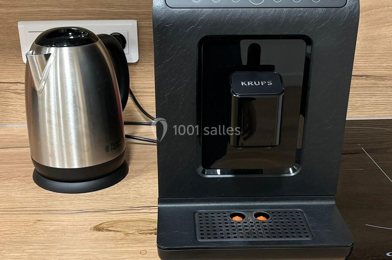 Bouilloire en acier inoxydable et machine à café noire posées sur un plan de travail en bois clair.