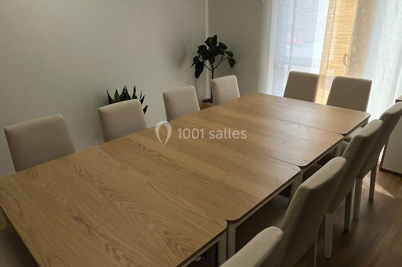 Table rectangulaire en bois clair entourée de chaises beige dans une pièce lumineuse avec des plantes en arrière-plan.