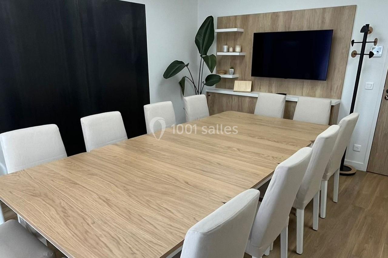 Salle de réunion avec une grande table en bois, chaises blanches, écran mural et décor minimaliste.
