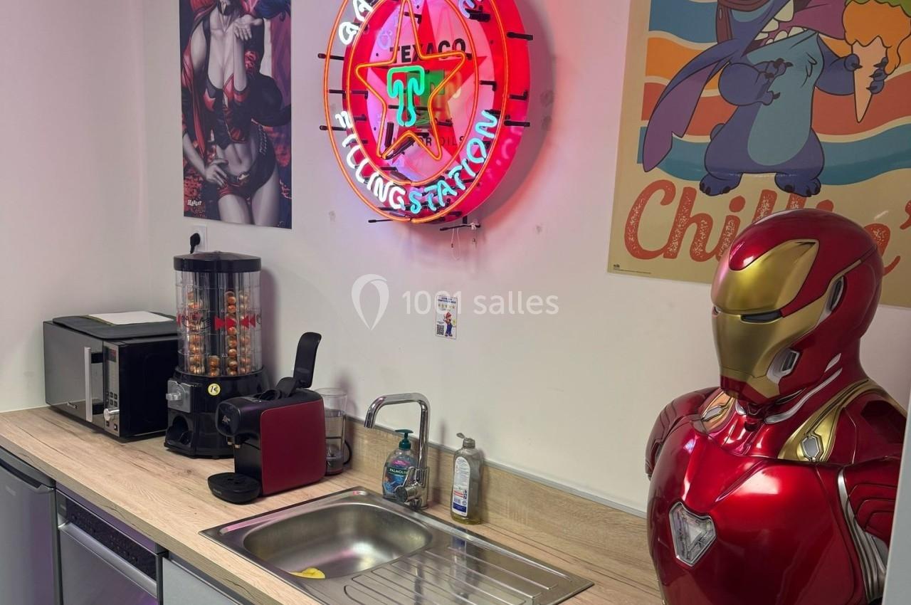 Cuisine avec évier, machine à café, distributeur de bonbons, affiche rétro et statue d'armure rouge et dorée.