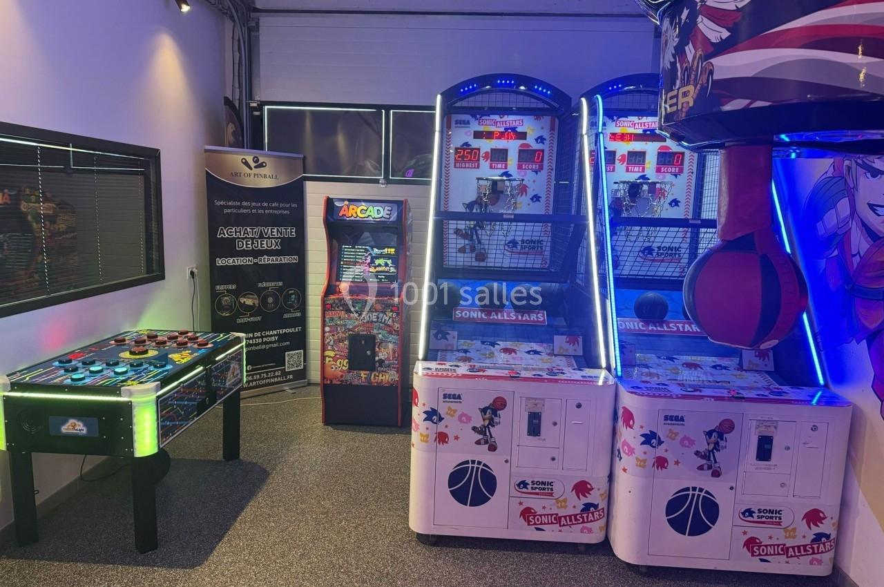Salle de jeux avec un baby-foot lumineux, des machines de basket arcade et un punching-ball, éclairée par des néons.