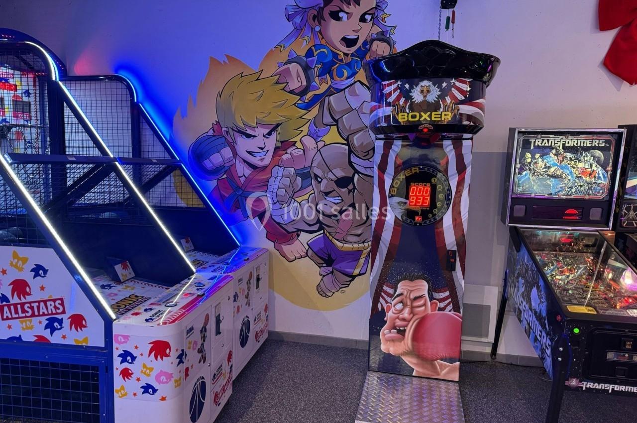 Jeu de boxe arcade entouré d'une machine de basket et d'un flipper, avec une fresque murale de personnages animés.