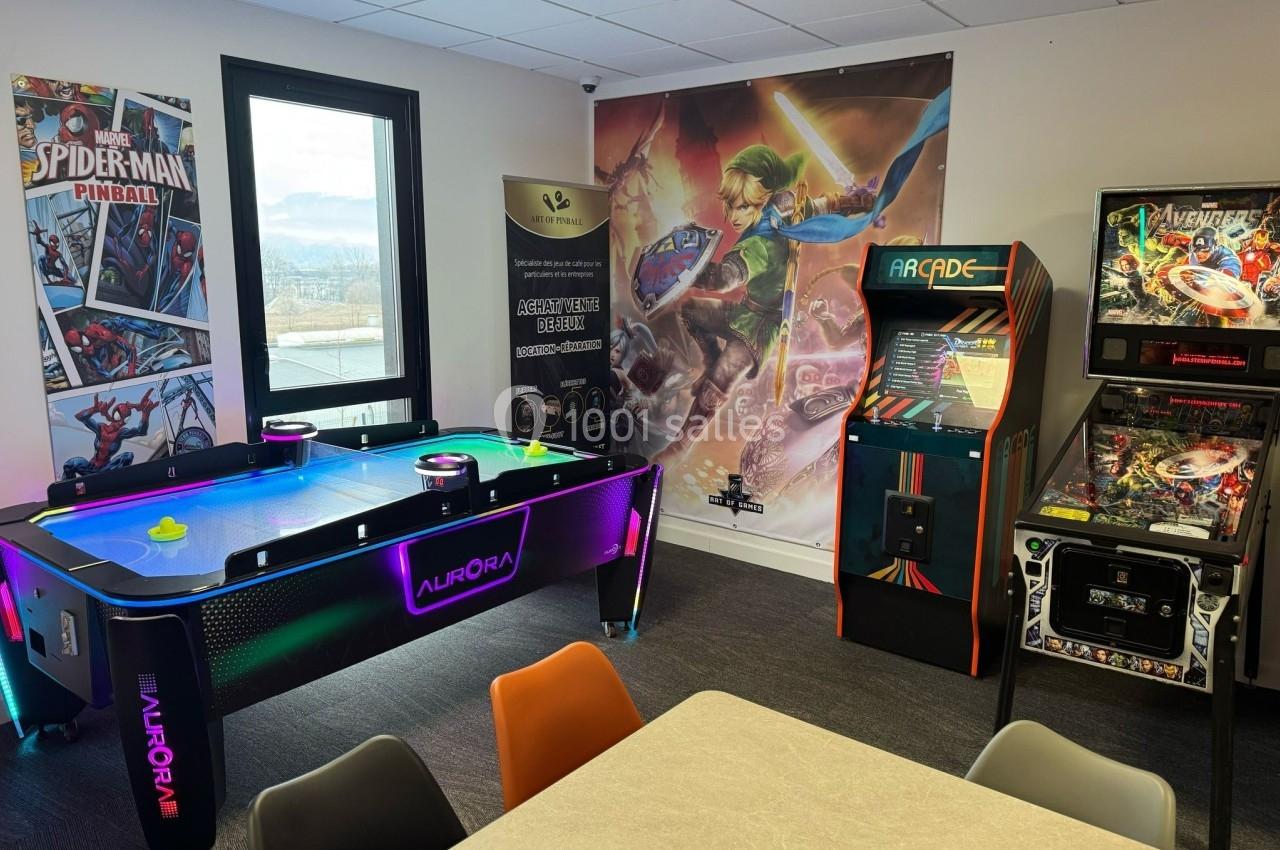 Salle de jeux avec une table de air hockey lumineuse, bornes d'arcade rétro et affiches décoratives sur les murs.