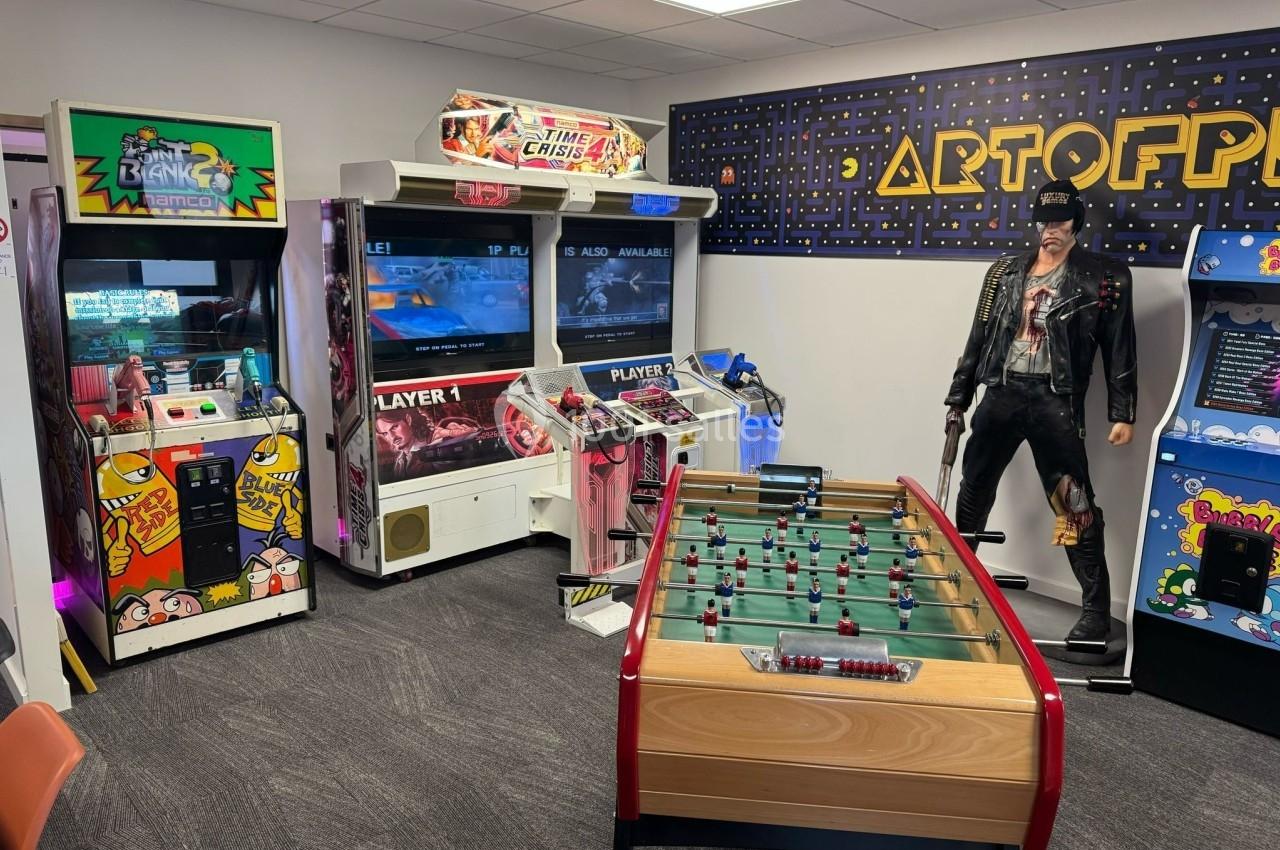 Salle de jeux rétro avec bornes d'arcade, baby-foot, statue décorative et décoration murale inspirée de Pac-Man.