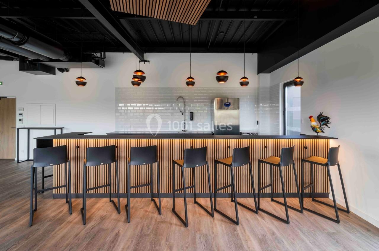 Comptoir de bar moderne avec tabourets noirs, éclairage suspendu et décor minimaliste dans un espace lumineux.