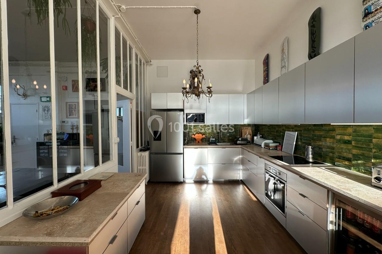 Cuisine moderne avec meubles blancs, plan de travail en bois, crédence verte et lumière naturelle traversant une verrière.