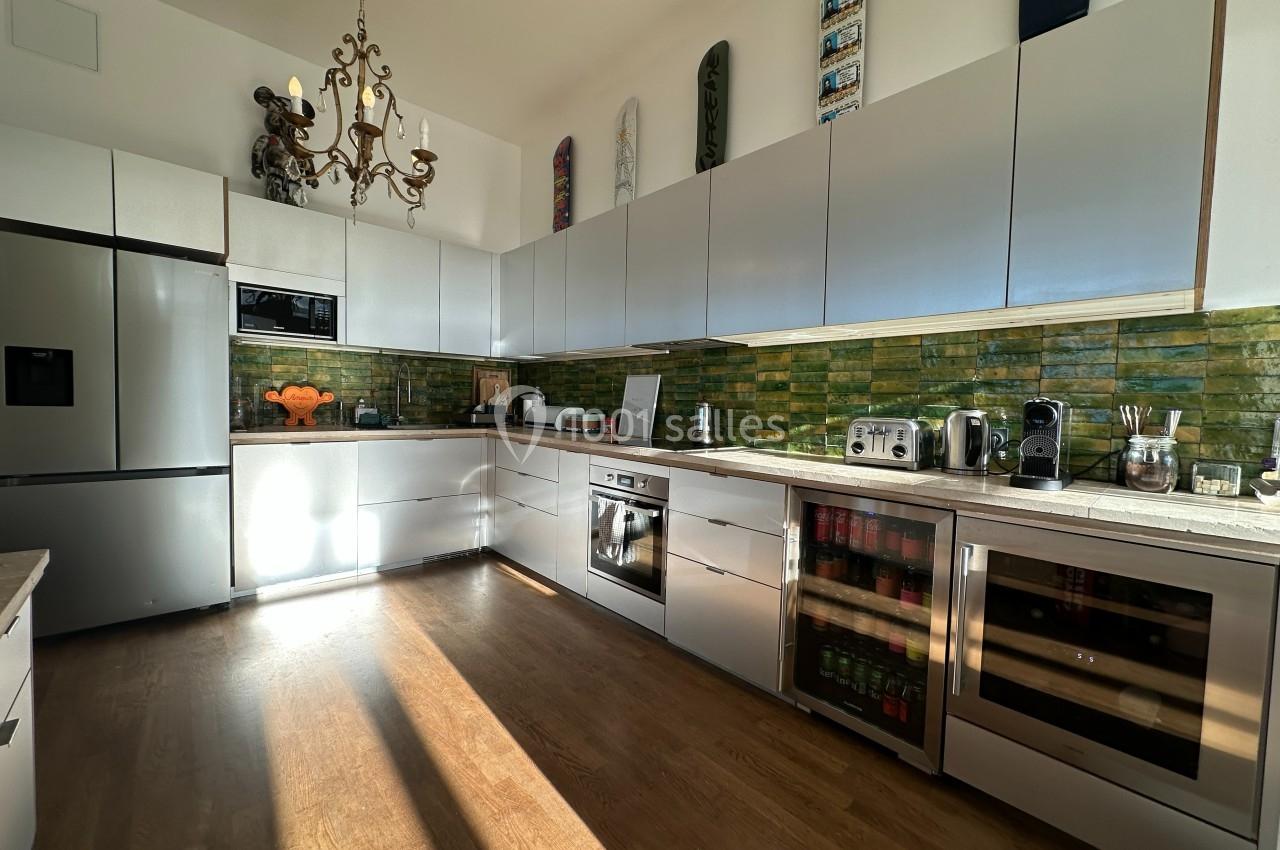 Cuisine moderne avec meubles blancs, plan de travail clair, crédence en carrelage vert et électroménagers en acier…