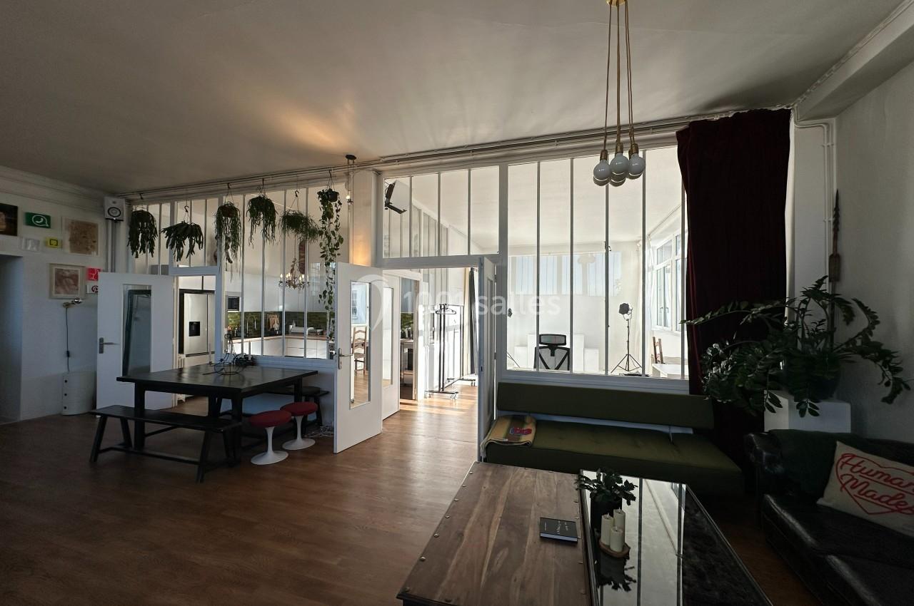 Espace intérieur lumineux avec verrière, mobilier moderne, plantes suspendues et coin salon.