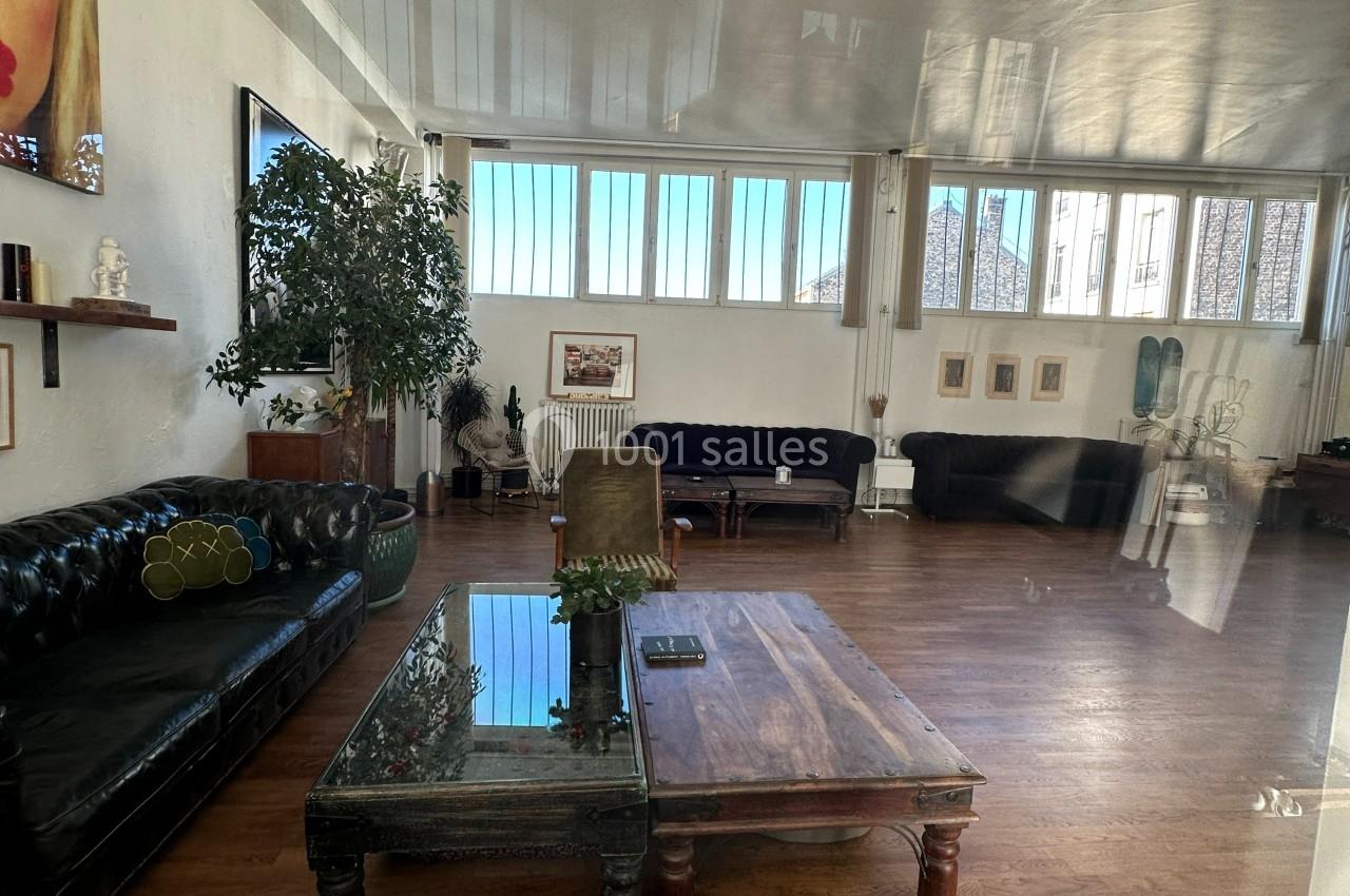 Salon spacieux avec parquet, canapés en cuir, tables en bois, plantes et grandes fenêtres laissant entrer la lumière…