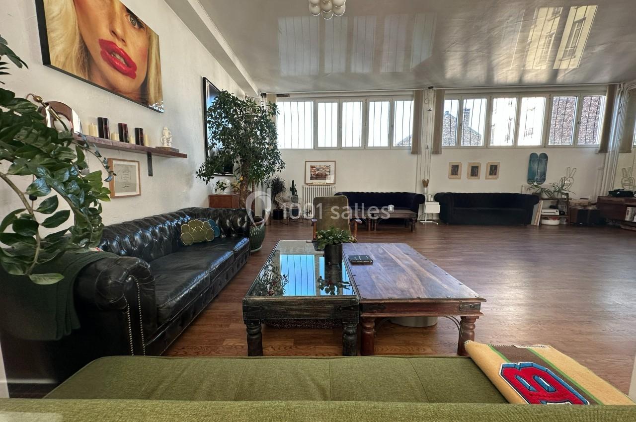 Salon spacieux avec canapés en cuir, table basse en bois, plantes et grandes fenêtres laissant entrer la lumière naturelle.