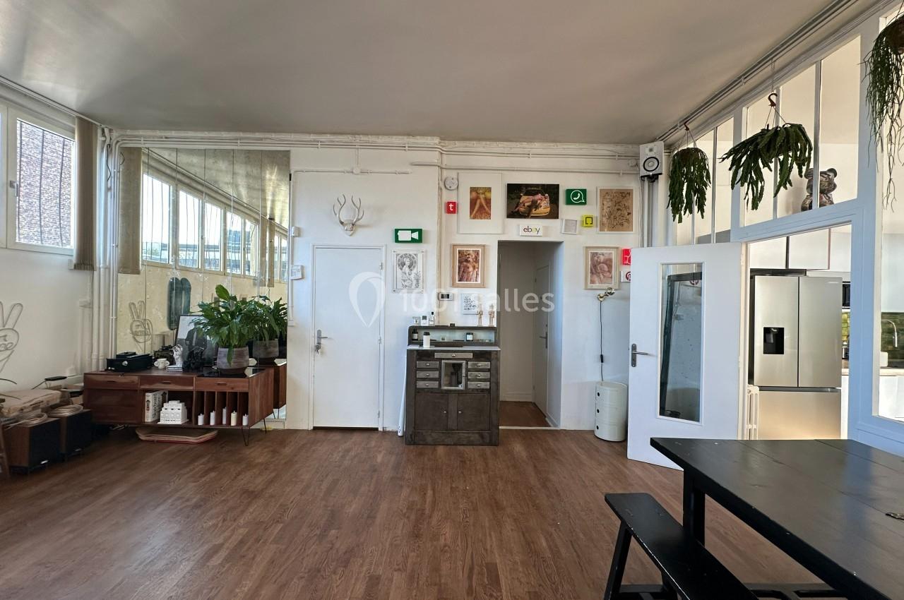Salle lumineuse avec parquet, kitchenette équipée, table en bois noir, plantes suspendues et décorations murales.