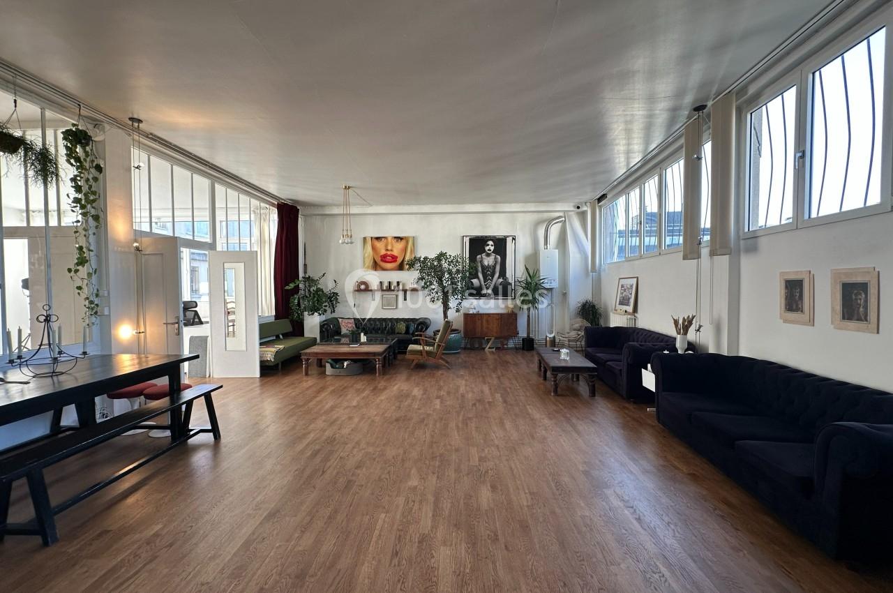 Salle spacieuse avec parquet, canapés, table en bois, plantes et grandes fenêtres laissant entrer la lumière naturelle.