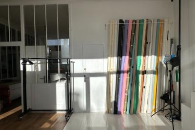 Salle lumineuse avec parquet, canapés sombres, plantes, décorations murales et grandes fenêtres laissant entrer la lumière.