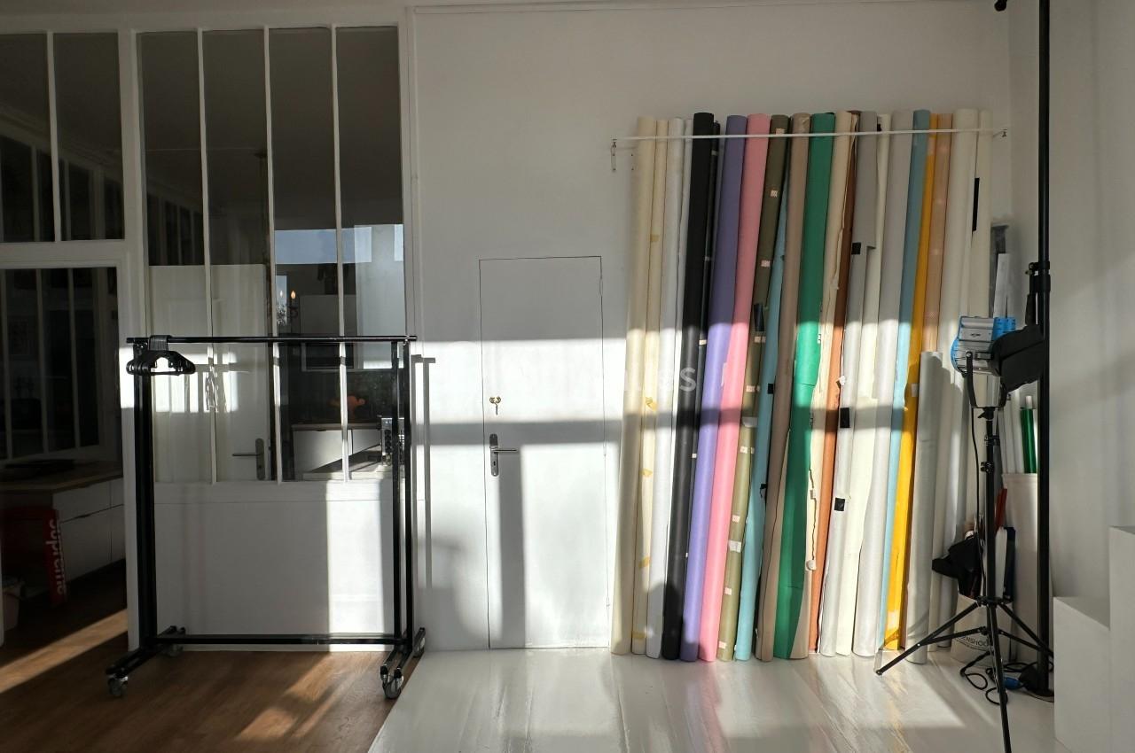 Mur blanc avec porte, supports de fonds colorés alignés à droite et équipement de studio photo à proximité.