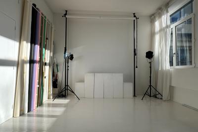 Salle lumineuse avec parquet, canapés sombres, plantes, décorations murales et grandes fenêtres laissant entrer la lumière.