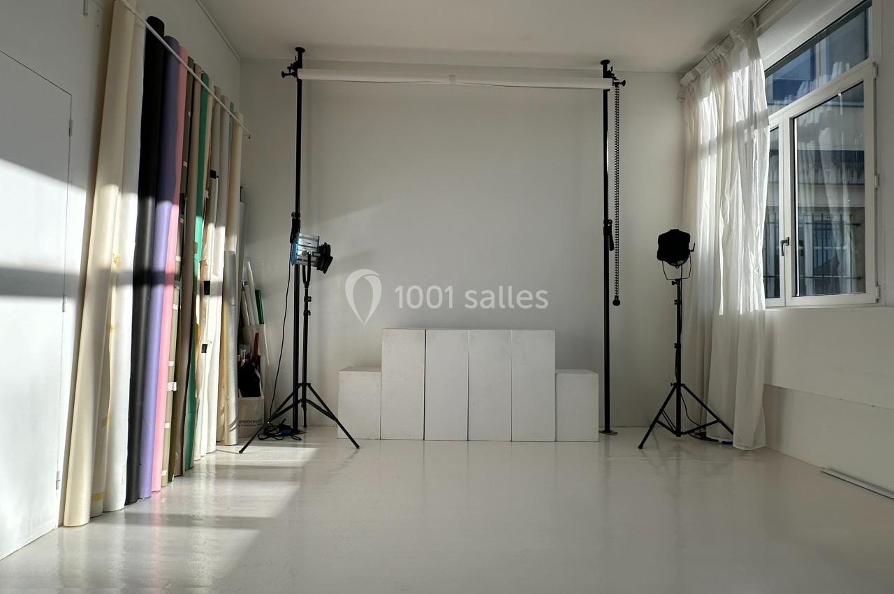 Studio photo lumineux avec fonds colorés, projecteurs sur trépieds et grandes fenêtres laissant entrer la lumière naturelle.