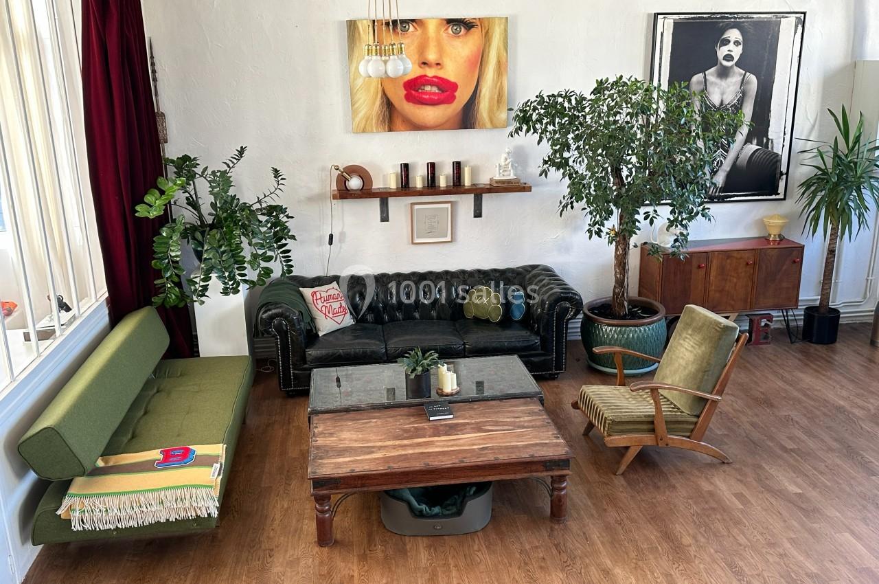 Salon lumineux avec canapé en cuir, fauteuils vintage, table basse en bois, plantes et œuvres d'art au mur.