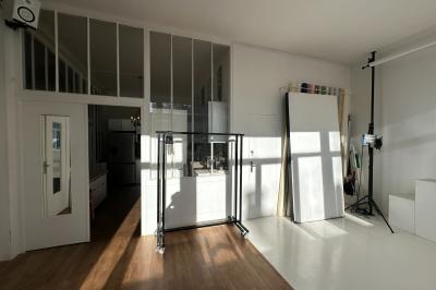 Salle lumineuse avec parquet, canapés sombres, plantes, décorations murales et grandes fenêtres laissant entrer la lumière.