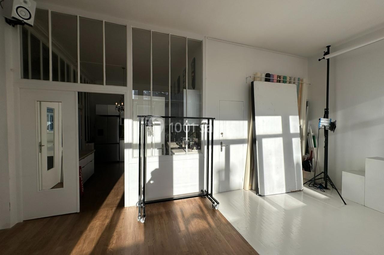 Intérieur lumineux d'un studio avec parquet, murs blancs, verrière, trépied et matériel de photographie.