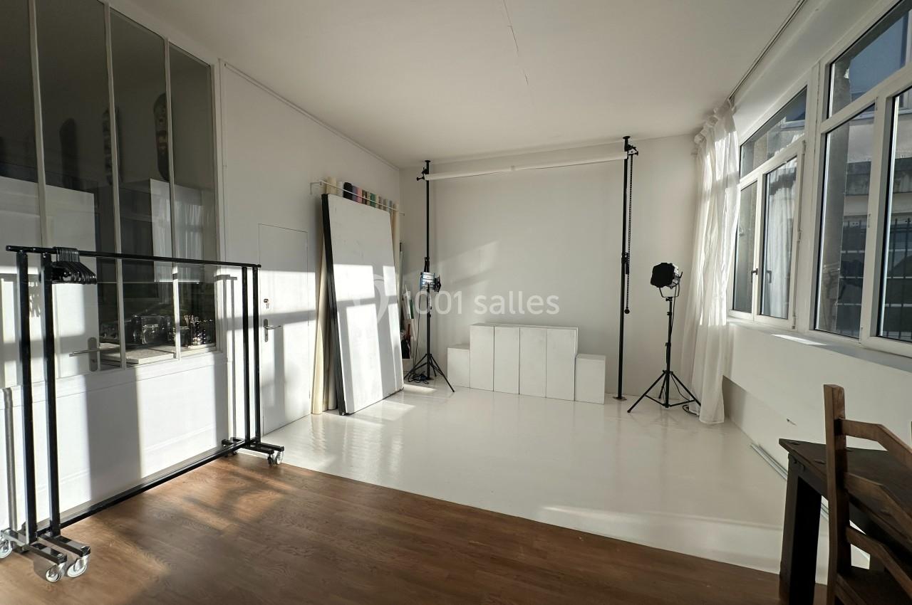 Studio photo lumineux avec parquet, fond blanc, éclairages professionnels et grandes fenêtres laissant entrer la lumière…