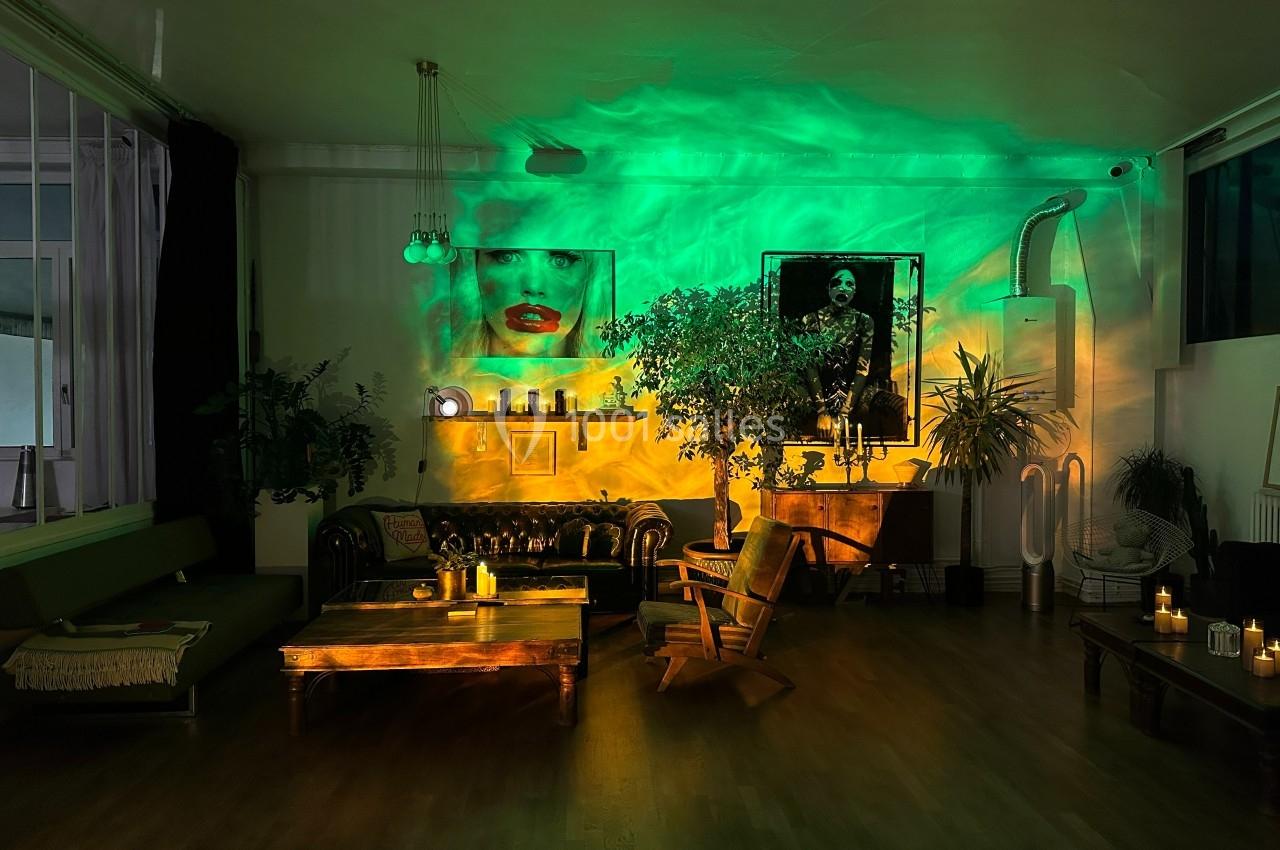 Salon avec éclairage tamisé vert et jaune, canapé en cuir, plantes, fauteuil en bois et décorations murales.