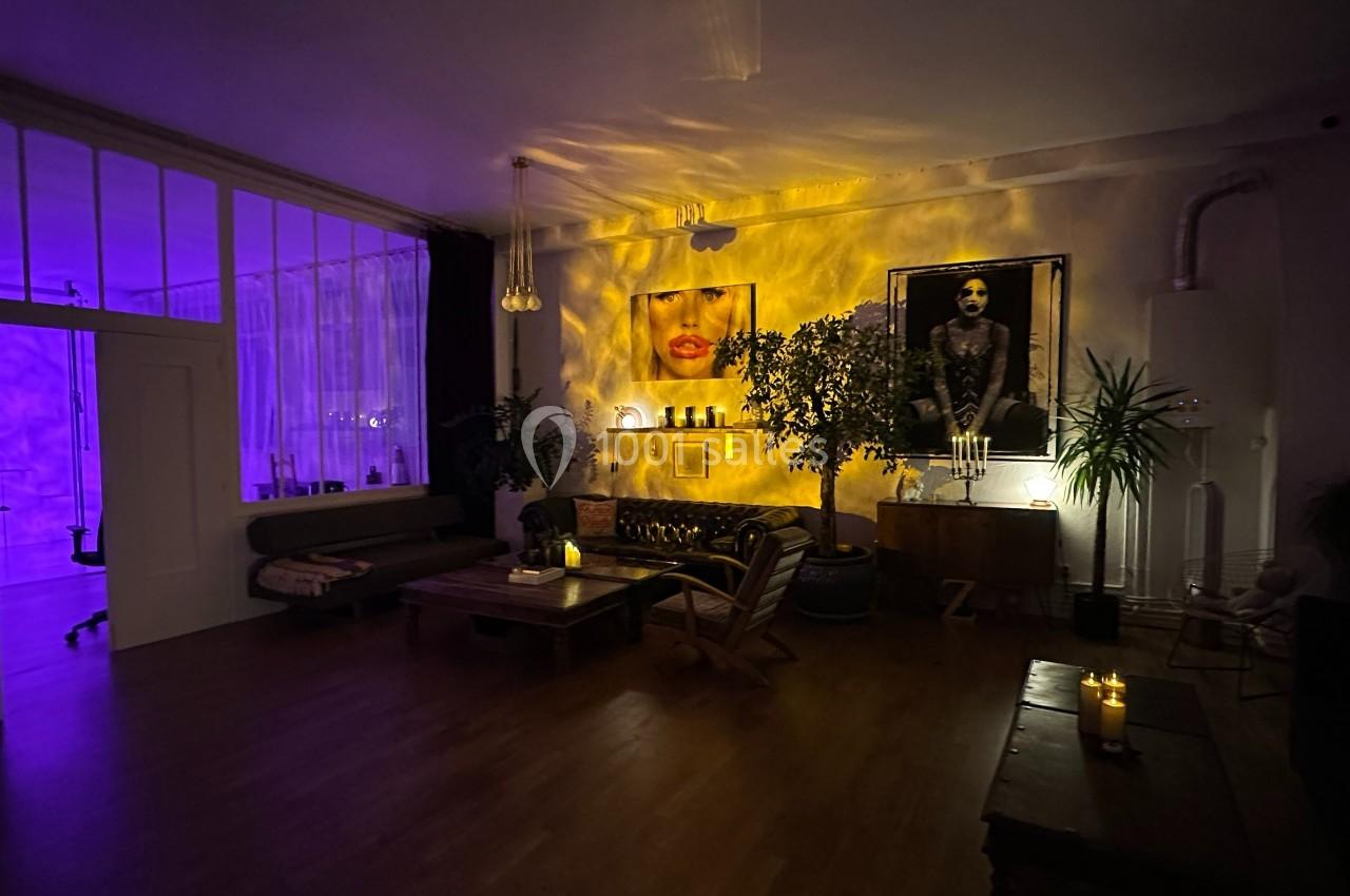 Salon cosy éclairé par des lumières tamisées, avec des plantes, des tableaux et des bougies sur des meubles en bois.