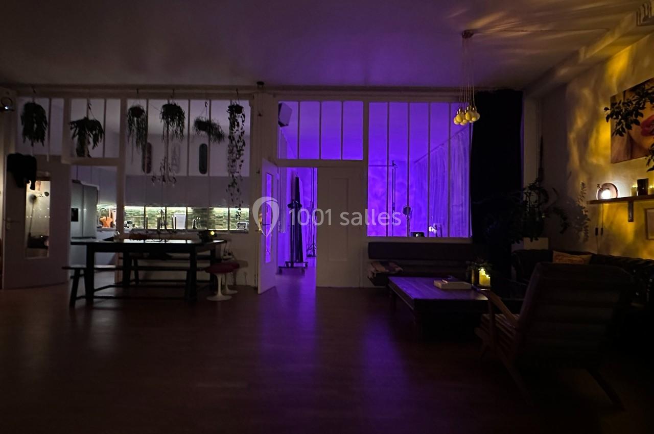 Intérieur d'une pièce sombre avec éclairage violet, mobilier moderne, plantes suspendues et ambiance chaleureuse.
