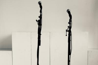 Salle lumineuse avec parquet, canapés sombres, plantes, décorations murales et grandes fenêtres laissant entrer la lumière.