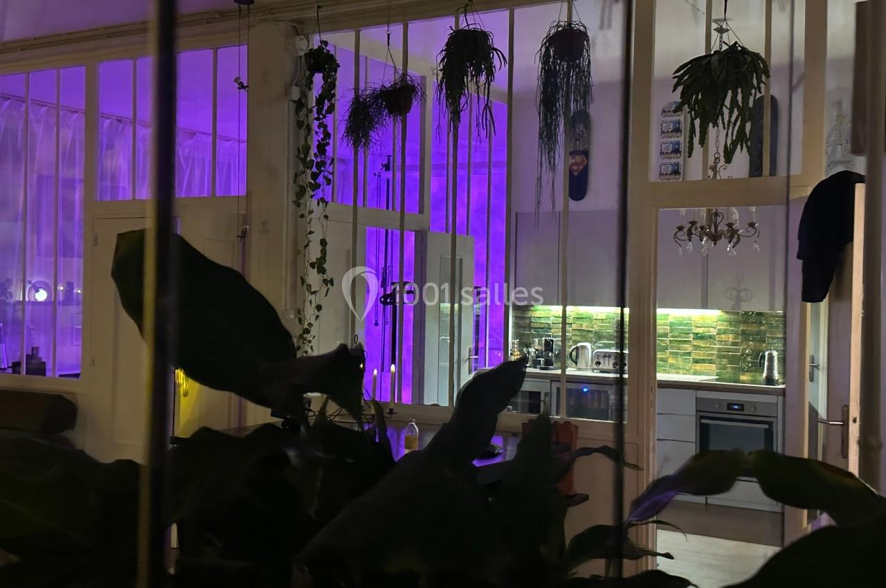 Vue d'une cuisine moderne éclairée par des lumières violettes, entourée de plantes suspendues et feuillues.