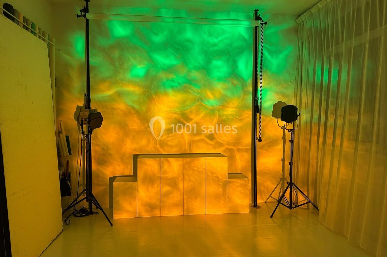 Studio avec éclairage coloré vert et jaune, deux projecteurs sur trépieds et rideaux blancs translucides en arrière-plan.