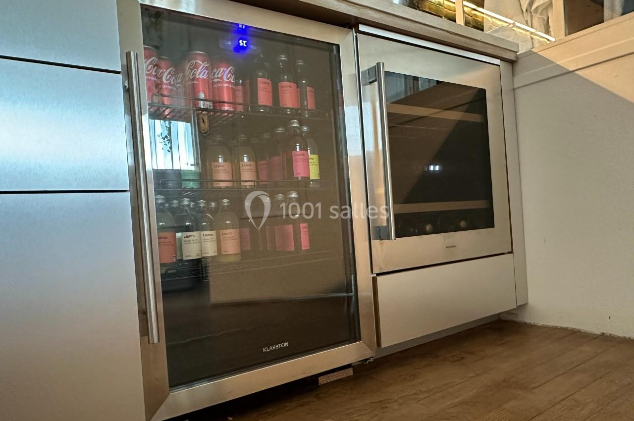 Réfrigérateur vitré intégré contenant des boissons, placé dans une cuisine moderne avec un sol en bois.