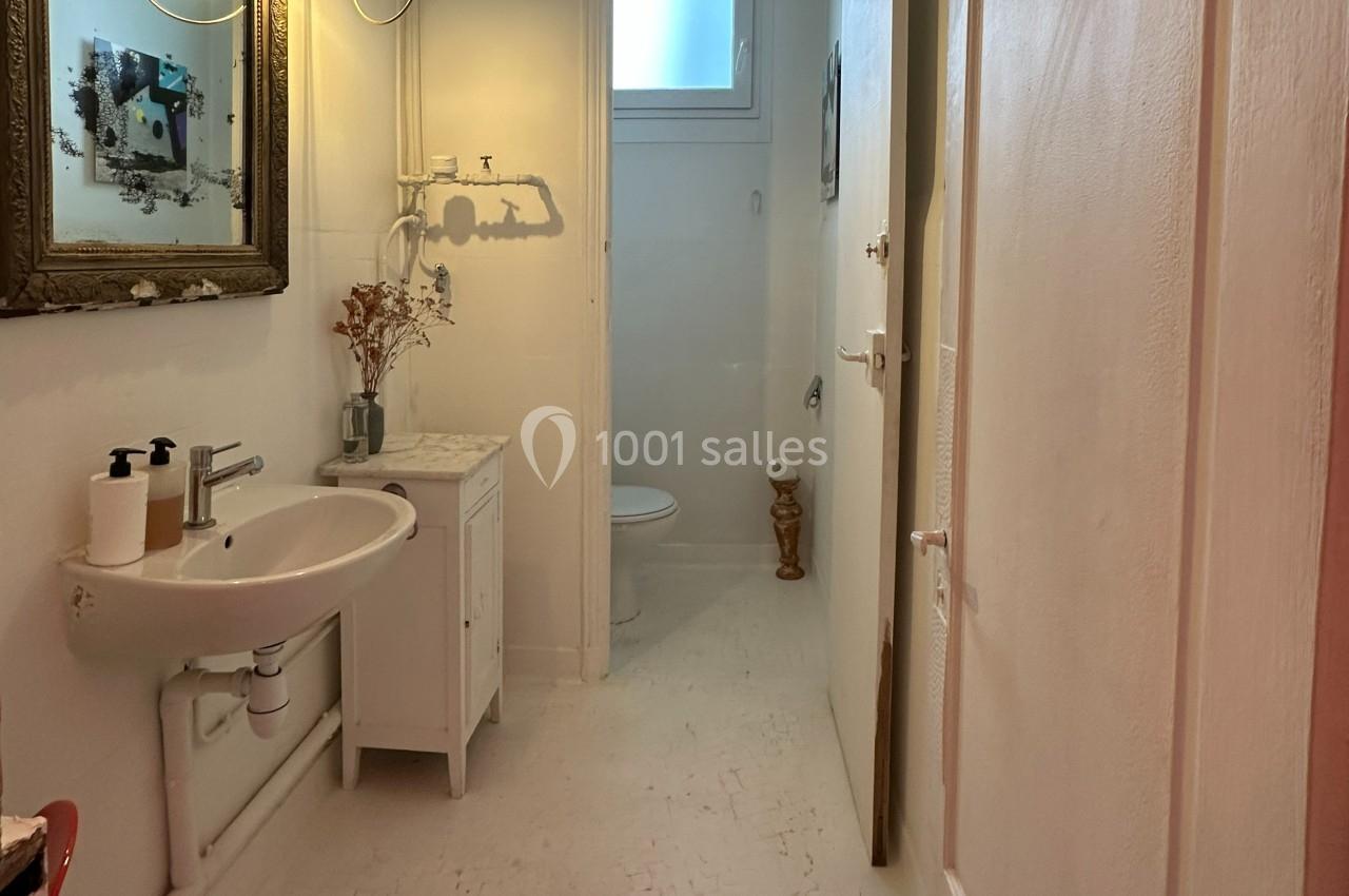 Salle de bain lumineuse avec lavabo, meuble blanc, miroir encadré, toilettes et petite fenêtre en hauteur.