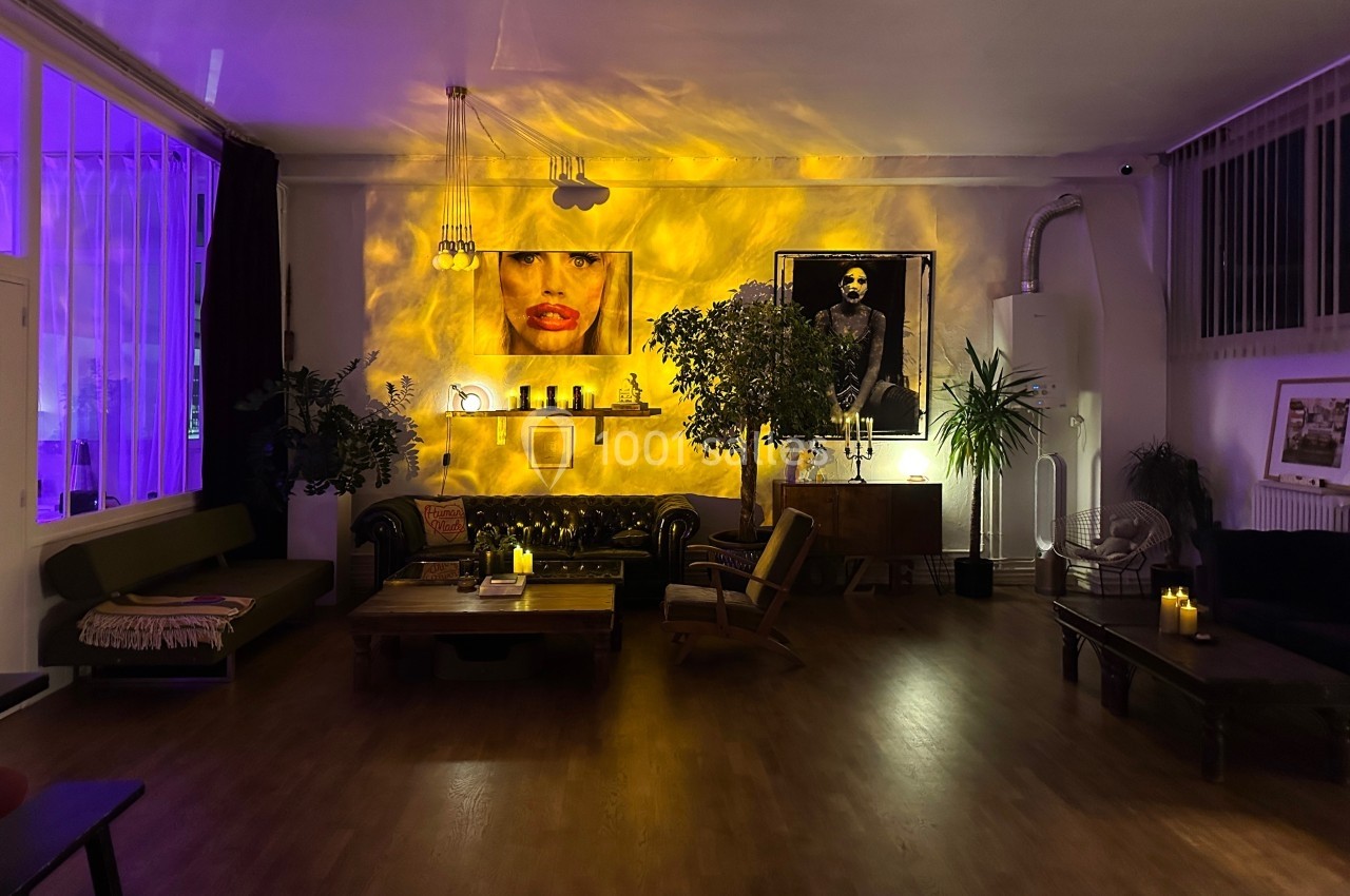 Salon cosy avec éclairage tamisé, canapés, plantes, tableaux au mur et bougies créant une ambiance chaleureuse.