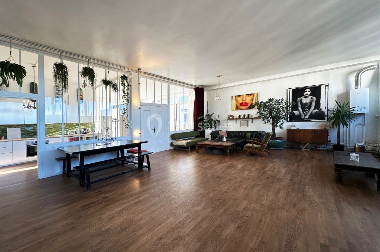 Espace de vie lumineux avec parquet, mobilier éclectique, plantes suspendues et grandes œuvres d'art sur les murs.