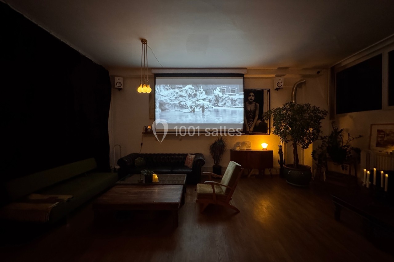 Salon sombre avec un projecteur affichant une image en noir et blanc, éclairé par des lampes et des bougies.