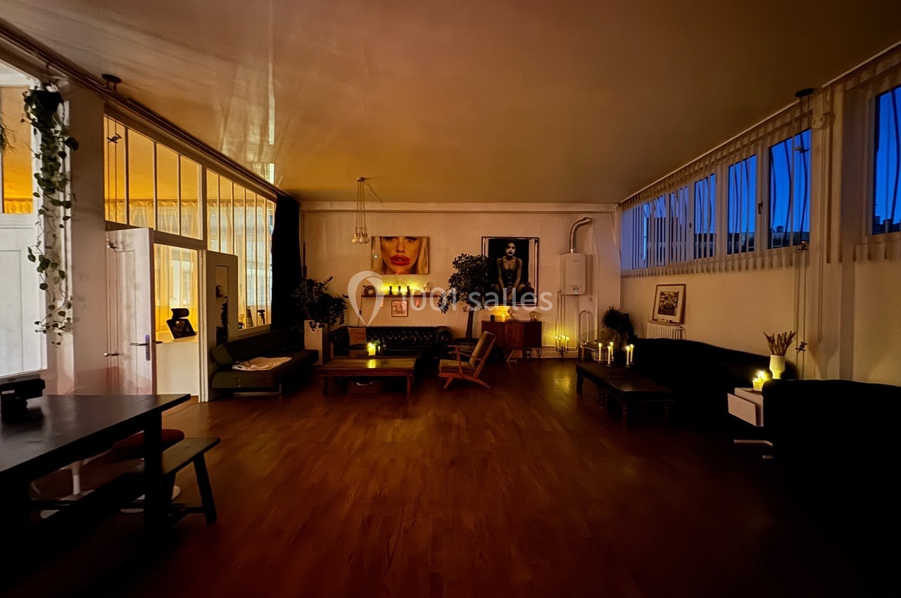 Salle de séjour spacieuse et tamisée, décorée de plantes, bougies et œuvres d'art, avec de grandes fenêtres.