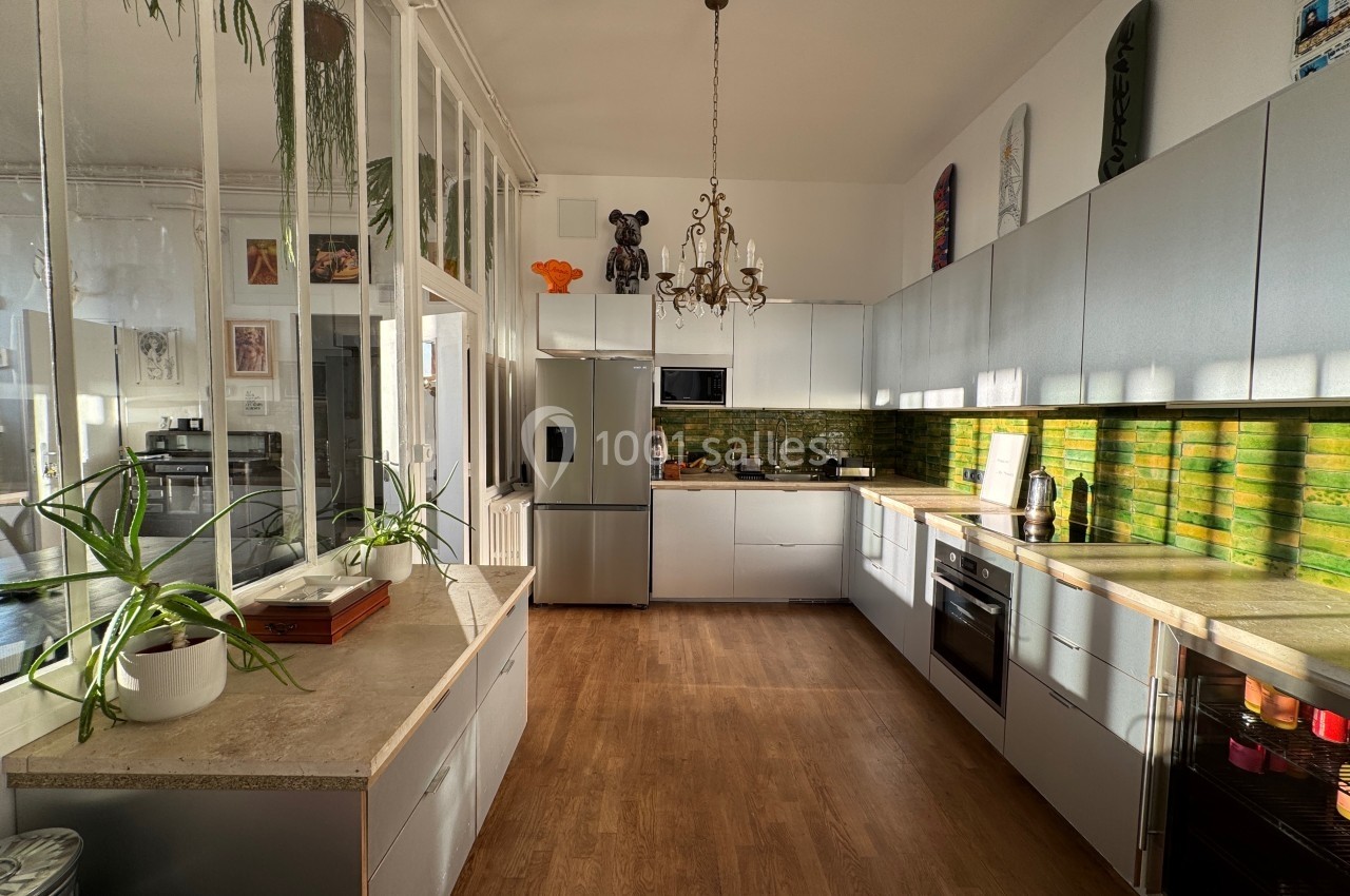 Cuisine moderne avec meubles blancs, plan de travail en bois, crédence verte et lumière naturelle entrant par de grandes…