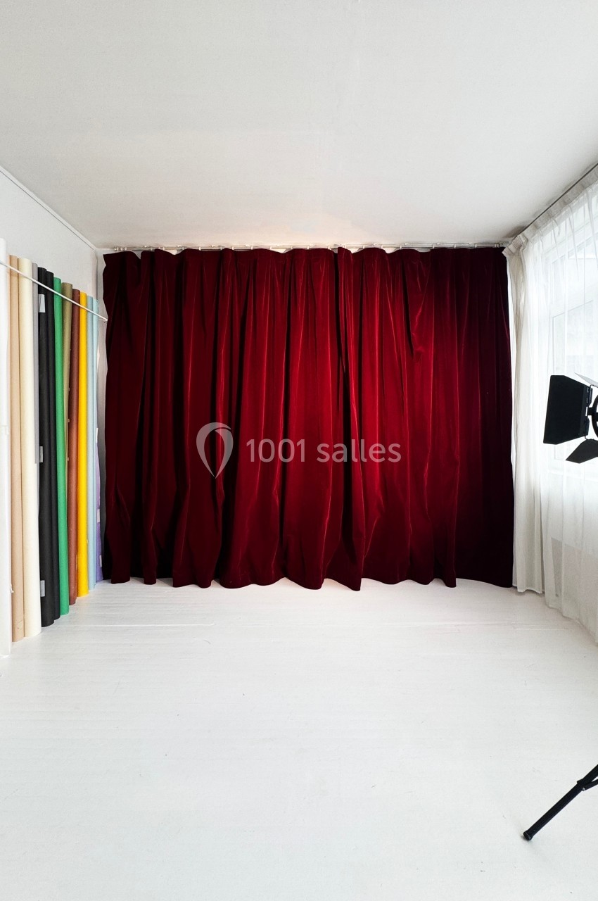 Rideau rouge épais couvrant un mur, éclairage de studio et rouleaux de tissus colorés alignés sur le côté.