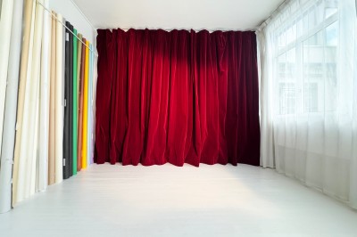 Rideaux rouges fermés dans une pièce lumineuse avec des échantillons de tissus colorés alignés sur la gauche.